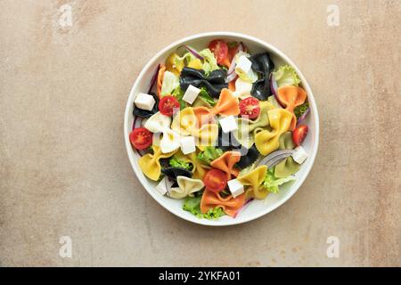 Blick von oben auf einen lebhaften Farfalle Pasta-Salat mit farbigen Nudeln mit Kurkuma, Spinat, Rote Bete, Paprika und Tintenfischtinte, gemischt mit Kirschtomaten Stockfoto