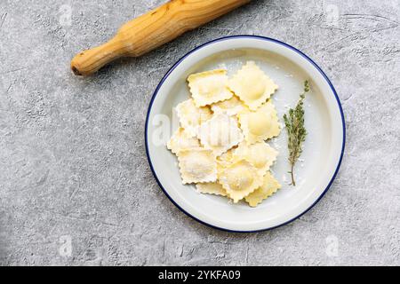 Ein Teller mit frisch zubereiteten Ravioli gefüllt mit Ziegenkäse und karamelisierten Zwiebeln, serviert und garniert mit Thymian auf einem rustikalen Steinhintergrund Stockfoto