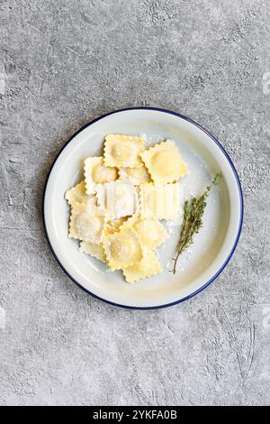 Ein Teller mit frisch zubereiteten Ravioli gefüllt mit Ziegenkäse und karamelisierten Zwiebeln und garniert mit Thymian auf einem rustikalen Steinhintergrund Stockfoto