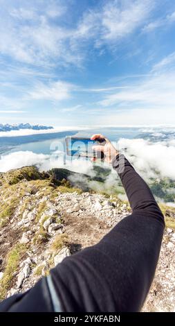 Ein Wanderer fängt die atemberaubende alpine Landschaft mit einem Smartphone am Rande des zerklüfteten Dent de Jaman in den Schweizer Alpen ein und zeigt die surreale Schönheit o Stockfoto