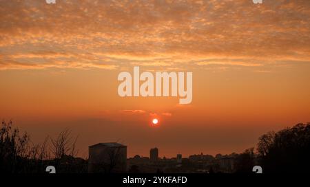 Ein atemberaubender urbaner Sonnenuntergang färbt den Himmel in leuchtenden Orangetönen die Sonne fällt hinter den Silhouetten der Stadt ab und strahlt ein warmes Leuchten über der Skyline von Wispy aus Stockfoto