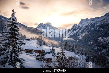 Atemberaubende Winterszene der Alpen bei Sonnenaufgang, mit schneebedeckten Bergen, malerischem Dorf und hohen Bäumen, die ruhige Atmosphäre unterstreicht die Natur Stockfoto