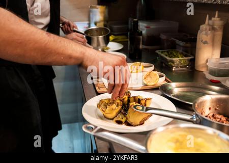 Zwei Köche garnieren und teller in einer belebten Restaurantküche sorgfältig herzhafte Gerichte, umgeben von einer Auswahl an Kochutensilien und frischen Zutaten Stockfoto