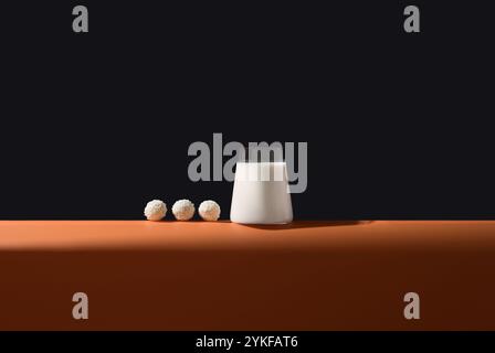 Modernes, minimalistisches Bild mit einem makellosen Glas Milch und drei Kokosstaubpralinen, die sich ordentlich vor tiefschwarzem Hintergrund und einem C aneinanderreihen Stockfoto