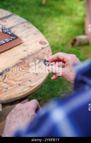 Ein abgeschnittener, nicht erkennbarer älterer Mann, der ein Domino-Stück hält, sich auf einen Holztisch fokussiert, um einen ruhigen Moment der Freizeit festzuhalten. Stockfoto
