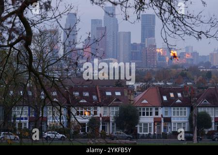 Durch die Baumzweige im Ruskin Park ist eine gemütliche Vorstadtbeleuchtung zu sehen, die mit dem orangen Sonnenaufgang übereinstimmt, der sich in einem entfernten Hochhaus am 16. November 2024 in London, England, in der wachsenden Siedlung Nine Elms spiegelt. Stockfoto