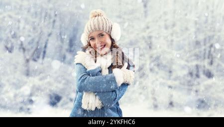 Glückliche Frau, die Winterschneefall draußen in der Natur genießt. Sie bewundert den fallenden Schnee während eines weißen Weihnachtsfestes. Einen kuscheligen blauen Pullover tragen, einen Bommel... Stockfoto