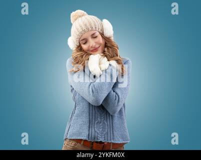 Fröhliche Frau, die sich in der Winterweihnachtszeit umschließt. Sie tragen einen kuscheligen blauen Pullover, eine Bommelmütze mit Ohrwärmern, Schal und Handschuhen. Sie sm Stockfoto