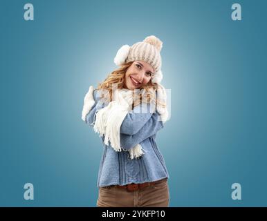 Fröhliche Frau, die sich in der Winterweihnachtszeit umschließt. Sie tragen einen kuscheligen blauen Pullover, eine Bommelmütze mit Ohrwärmern, Schal und Handschuhen. Sie sm Stockfoto
