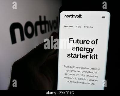 Deutschland. August 2024. In dieser Abbildung hält ein Mann ein Smartphone mit der Website des schwedischen Batterieunternehmens Northvolt ab vor dem Firmenlogo. Quelle: SOPA Images Limited/Alamy Live News Stockfoto