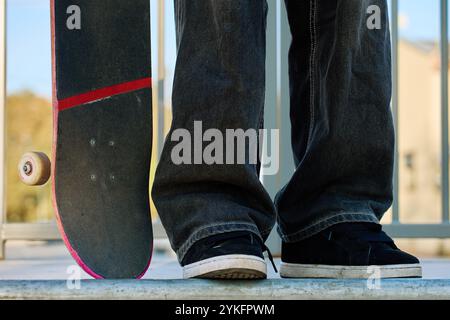 Skateboarder in Baggy-Jeans mit einem zerkratzten rosa Skateboard auf der City Street. Der Teenager ist Skateboarding. Konzept der Jugendsubkultur Stockfoto