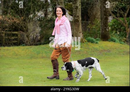 Eine Frau mittleren Alters, die mit ihrem älteren Cocker Spaniel Hund läuft. Stockfoto
