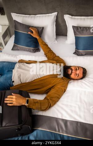 Junger glücklicher Mann ist im Urlaub. Tourist kam im Hotelzimmer an und entspannte sich auf dem Bett. Stockfoto