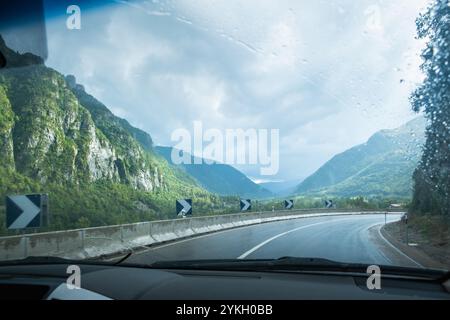 Eine nasse Straße an einem bewölkten und regnerischen Tag aus dem Inneren eines Fahrzeugs. Es gibt eine scharfe Kurve, die gut ausgeschildert ist. Konzept von Fahren, Transport und Cautio Stockfoto