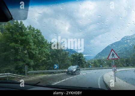 Eine nasse Straße an einem bewölkten und regnerischen Tag aus dem Inneren eines Fahrzeugs. Es gibt ein Auto in die entgegengesetzte Richtung und eine Fußgängerüberfahrt. Konzept von Stockfoto