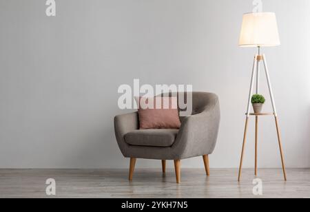 Bequemer Sessel mit rosa Kissen, leuchtende Lampe auf dem Boden auf grauem Wandhintergrund im Büro oder Wohnzimmer Stockfoto