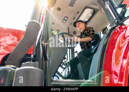 Tiefwinkelansicht einer jungen erwachsenen Kaukasain-Landarbeiterin, die im Betrieb Traktor fährt. Stockfoto