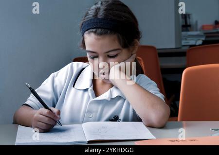 GELANGWEILTES KLASSENZIMMER SCHÜLERIN JUNIOR Junior Schulmädchen 7-10 Jahre in Uniform müde gelangweilt, desinteressiert an ihrem Studium an ihrem Schreibtisch im Klassenzimmer Stockfoto