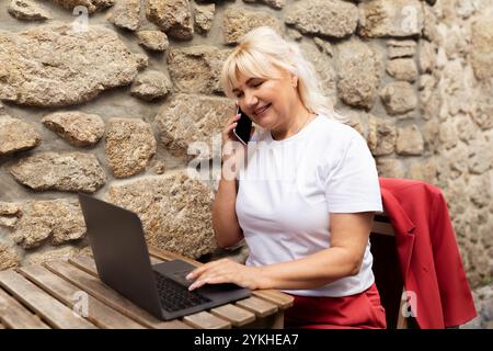 Frau benutzt ihren Laptop und spricht am Telefon in einem rustikalen Café Stockfoto