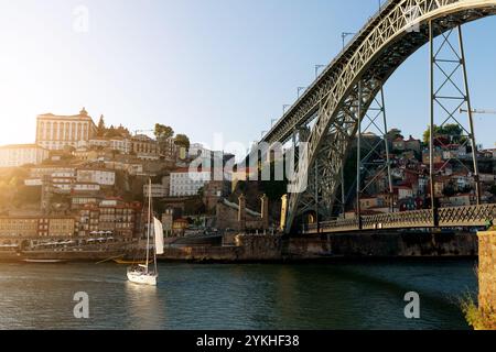 Segelboot gleitet unter der berühmten Brücke von Porto bei Sonnenuntergang mit farbenfrohen Häusern Stockfoto