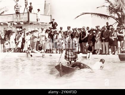 Die Zuschauer in Miami, Florida, versammelten sich um einen Pool, wo ein Seminolenindianer in einem Kanu steht, während ein anderer Mann am 4. März 1922 mit einem Alligator im Wasser neben dem Kanu kämpft. (USA) Stockfoto