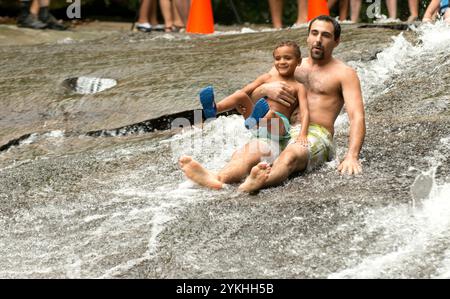 David und sein Sohn Preston Dougherty rutschen auf dem Sliding Rock im Pisgah National Forest, NC. Sliding Rock ist eine 60 Meter lange, rutschige Kaskade in den 50-60 Grad tiefen Pool. Es gibt 2 Aussichtsplattformen und Rettungsschwimmer im Dienst während der Saison. Dies ist ein stark genutztes Naherholungsgebiet, das sich oft voll ausfüllt. Personen, die am Straßenrand außerhalb des ausgewiesenen Parkplatzes parken, erhalten ein Ticket. Es wird auch empfohlen, alte Shorts und Turnschuhe zu tragen, wenn du dich für den Sprung entscheidest. Der Eintritt kostet 2,00 $ pro Person für Schieber und Beobachter. (Foto des Forstdienstes b Stockfoto