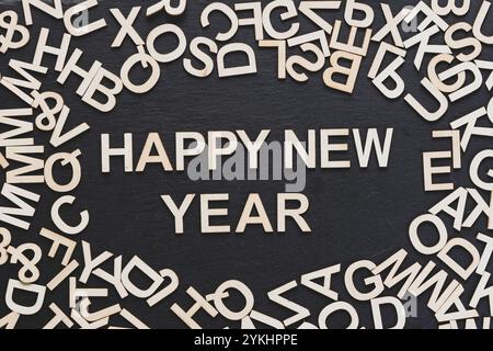Auf dem Bild sehen Sie viele Holzbuchstaben, die auf einem Tafel-Hintergrund verstreut sind, und in der Mitte eine frohes neues Jahr-Phrase Stockfoto