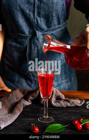 Die Hand einer Frau gießt Kirschlikör in ein Glas. Hausgemachter Kirschlikör. Stockfoto