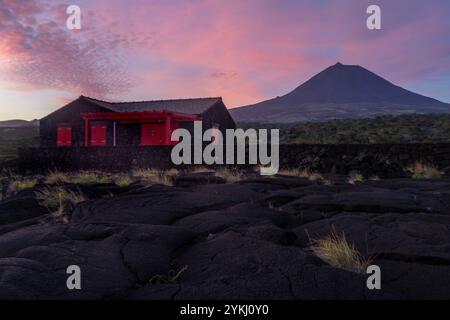 Cabrito auf der Insel Pico auf den Azoren hat einen Badebereich aus schwarzer Lava mit traditionellen Lavasteinhäusern mit Blick auf den majestätischen Mount Pico. Stockfoto