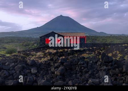 Cabrito auf der Insel Pico auf den Azoren hat einen Badebereich aus schwarzer Lava mit traditionellen Lavasteinhäusern mit Blick auf den majestätischen Mount Pico. Stockfoto