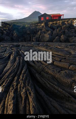 Cabrito auf der Insel Pico auf den Azoren hat einen Badebereich aus schwarzer Lava mit traditionellen Lavasteinhäusern mit Blick auf den majestätischen Mount Pico. Stockfoto