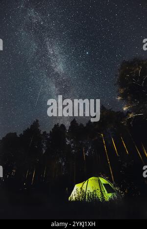 Ein leuchtend grünes Zelt, eingebettet in einen Wald unter der atemberaubenden Milchstraße, bietet eine perfekte Kulisse für eine ruhige Nacht mit Camping und Sternenbeobachtung Stockfoto