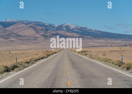 U.S. Route 50, die einsamste Straße der USA, bietet einen Blick auf schneebedeckte Berge. Leere Straße und klarer blauer Himmel. Stockfoto