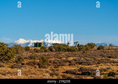 ÖlPumpjack und Lagertanks in einer Wüstenlandschaft nahe Moab, Utah, mit den schneebedeckten La Sal Mountains unter einem klaren blauen Himmel Stockfoto