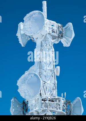 Mikrowellengeschirr und Radioantenne auf einem Berg, bedeckt mit Schnee und Eis, mit blauem Himmel Hintergrund Stockfoto