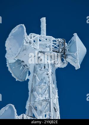 Mikrowellengeschirr und Radioantenne auf einem Berg, bedeckt mit Schnee und Eis, mit blauem Himmel Hintergrund Stockfoto