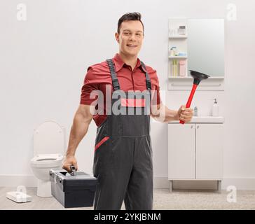 Klempner im Badezimmer, der Werkzeuge hält und lächelt Stockfoto