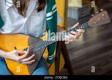 Mädchen, das zu Hause auf russischer Balalaika spielt, Nahaufnahme der Hände und Saiten Stockfoto