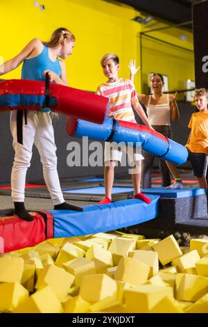 Glückliche Kinder Schuljunge und Teenager Mädchen kämpfen an aufblasbaren Baumstämmen, während sie ein Wochenende zusammen im Entertainment Center verbringen Stockfoto