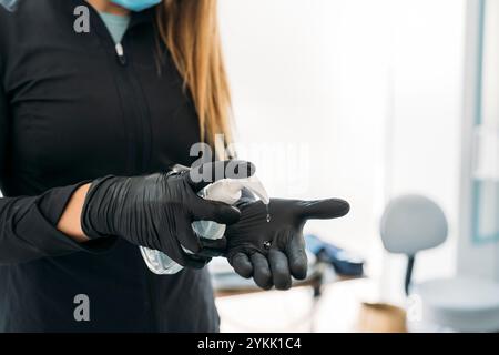 Kosmetikerin mit schwarzen Handschuhen, die Hände mit hydroalkoholischem Gel desinfizieren Stockfoto