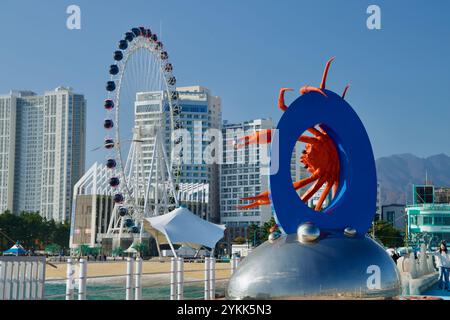 Sokcho, Südkorea - 3. November 2024: Das Sokcho Eye Ferris Wheel und die lebendige Krabbenskulptur stehen vor modernen Wolkenkratzern und dem Stockfoto