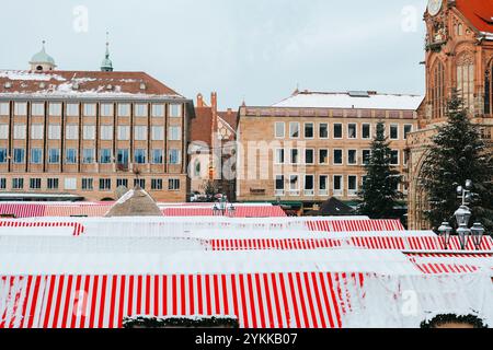 Weihnachtsmarkt in Nürnberg heben sich Zelte mit gestreiften Dächern von der verschneiten Landschaft ab. Festliche traditionelle Wintermesse Stockfoto