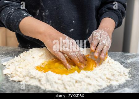 Nahaufnahme der Hände der jungen Frau, die Eier und Mehl auf einem Tisch in der Küche mischten Stockfoto