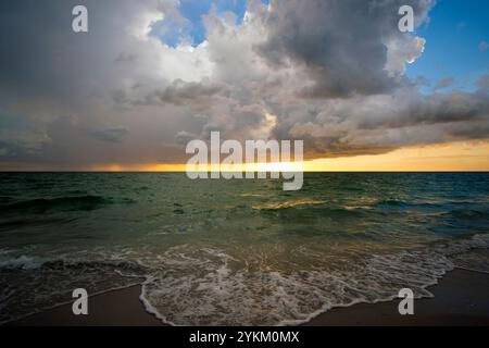 Ozeanlandschaft mit Gewitterwolken über rauen abendlichen Meerwasserwellen, die am Sandstrand zerquetschen. Wunderschöne Meereslandschaft bei Sonnenuntergang Stockfoto