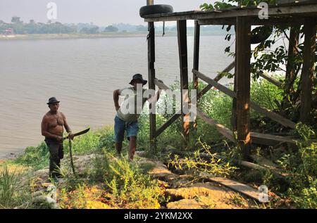 Zwei Männer stehen am Fuße eines Docks in Santa-Maria do Tapara, Brasilien. Während der Regenzeit steigt der Fluss bis zum Dock. Zwischen September und November 2023 erlebte das Amazonasgebiet eine beispiellose Dürre. Brände, die Flora und Fauna verwüsteten, und viele Gemeinden waren vom Rest der Welt abgeschnitten, denn für ihre Navigation sind sie auf ausgetrocknete Wasserstraßen angewiesen. Stockfoto