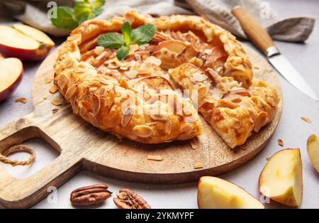 Frisch gebackene Apfelgalette, dekoriert mit Mandelflocken und Minzblättern, serviert auf einem Holzbrett Stockfoto