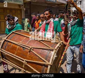 Ein Mann in traditioneller Kleidung spielt bei einem lebhaften Straßenfest in indien energisch eine große Trommel Stockfoto