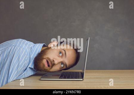 Blick von der Seite eines fokussierten Mannes, der sein Ohr auf das Notebook legt und dessen Geräusche aufmerksam hört. Stockfoto