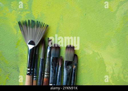 Eine Nahaufnahme von Pinseln, die auf einer Leinwand liegen, mit einer wunderschönen Mischung aus grüner, weißer und goldener Acrylfarbe. Stockfoto