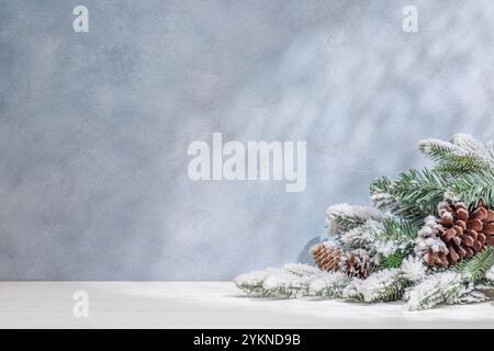 Weihnachtsschablone mit verschneiten Tannenzweigen auf einem Tisch mit Schatten und Sonnenstrahlen, die sanft an die Wand fallen, schaffen ein festliches Winterambiente Stockfoto